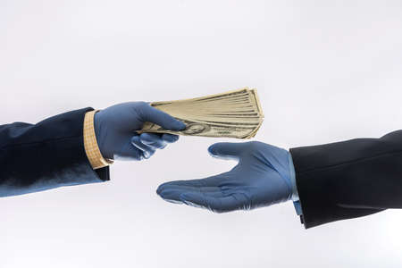 Two male hands in blue medical gloves with 100 dollar banknote, isolated. Concept of corruption or ray at quarantineの写真素材