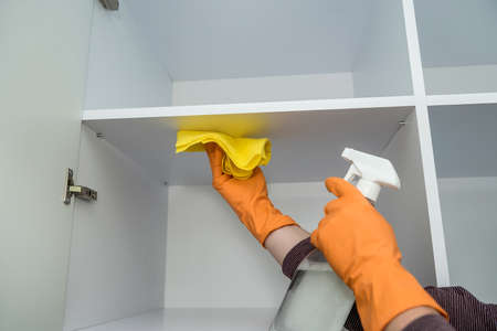 Hand in orange protective gloves with rag washing and spray cleaning kitchen furniture. Hygiene at homeの写真素材
