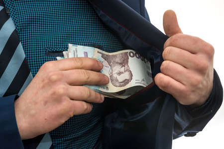 businessman takes a pack of Ukrainian money as a bribe and hides in his pocket in a jacket. Corruption and a trick. UAH. 1000 new banknoteの写真素材