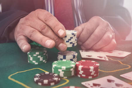 Man in casino looking at playing cards and stack of token chips. Gambling concept