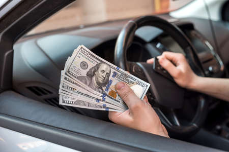businessman pays for a product or service, gives dollars while sitting in the car. finance conceptの写真素材