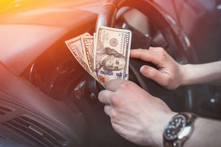 Man holding dollars sitting in car. buy or rent, bribe