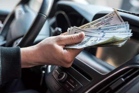 businessman pays for a product or service, gives dollars while sitting in the car. finance conceptの写真素材