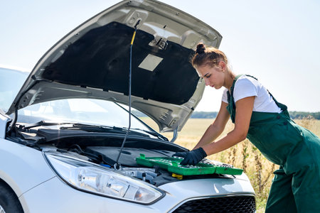Beautiful woman in overalls with the keys repairing a broken car in her journeyの写真素材