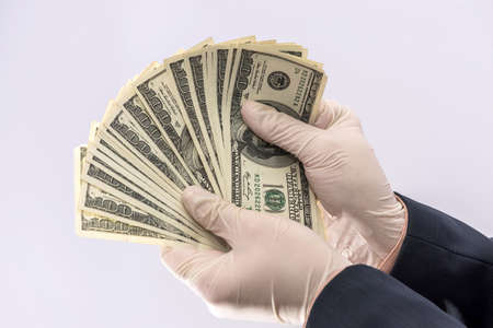 Male hand in medical glove holds us money bills for protection against Covid-19 (Coronavirus)...