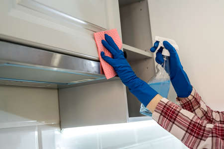 female hand in rubber protective cleaning cooker hood with rag in kitchen.