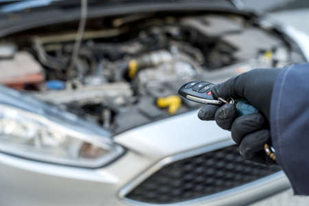Auto service mechanic hold keys in hand with car on the background, open hood. Repairの写真素材