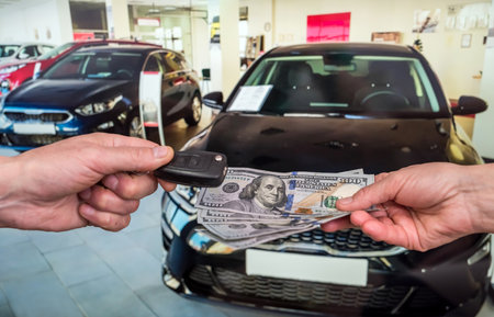 Male hand gives money and take car keys, new car as background. financeの写真素材