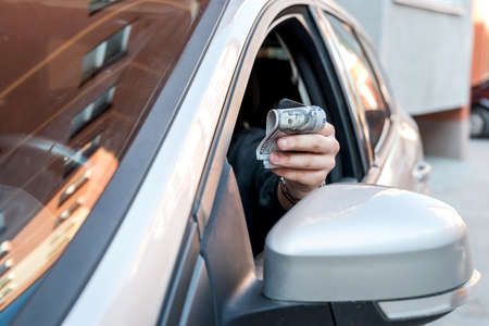 man in car holding dollar for bribe or pay in goods. business finance concept