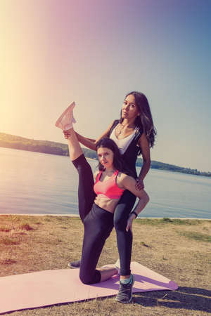 young slim women doing stretching exercise relaxing and warm up after jogging and running in park near lake, morning time. Concept of wellness and healthy lifestyleの写真素材