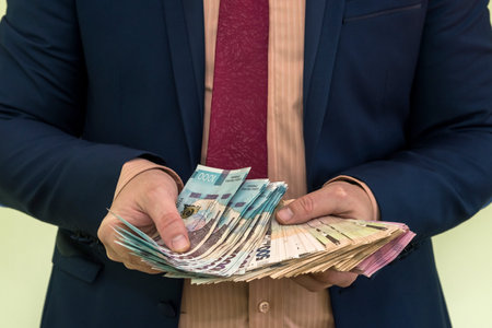 A man in a suit holds a large pile of Ukrainian money and shows his income. UAH. new banknotes 1000 and 500 hryvniaの写真素材