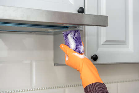 male hands in protective gloves cleaning the kitchen hood with rag and spray bottle . housekeeper