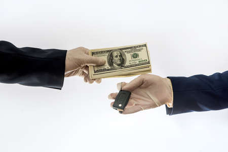 car sales in quarantine conditions virus hands holding car key and dollar bills isolated. Buying car...