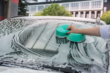 Female hands hold with green sponge and foam washing her car. cleaning concept.