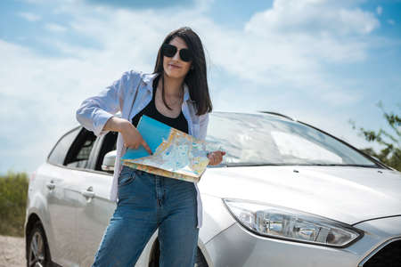 Pretty woman see the map near car in road. Concept of summer travel, freedom from the coronavirus...