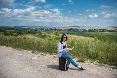 Woman tourist sitting on her luggage and look the map for choose best away. Summer active lifestyle conceptの写真素材