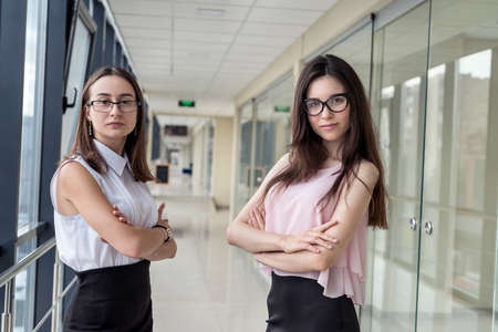 Two young business woman partners or agents standing inside building while discussing presentation at meetingの写真素材