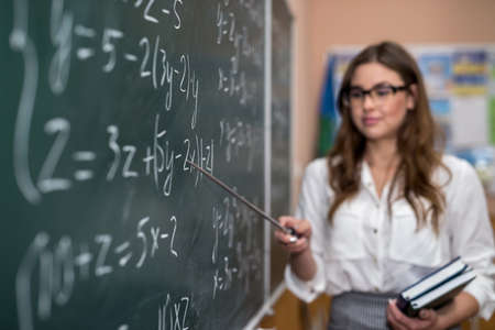 Young college student writing mathematical exercise on the chalkboard during a class. Education
