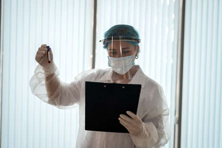 doctor looks at the results of the laboratory test in the clipboard and holds a test tube with blood covid19の写真素材