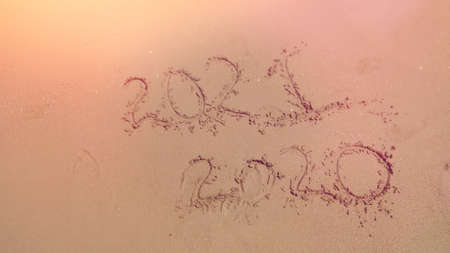 handwritten inscription 2020 and 2021 on sand of sea beach. background