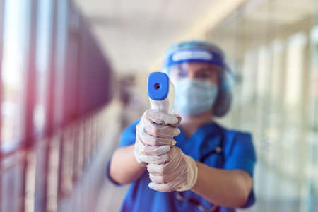 Female doctor wearing protective mask and face shield using infrared thermometer to check body temperature in clinic. covid19の写真素材