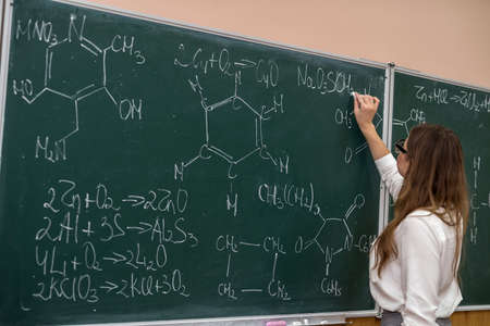Young funny female teacher in glasses against chalk blackboard with scientific formulas. chemistryの写真素材