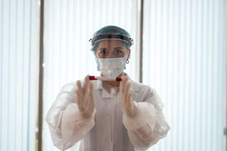 female nurse wearing protective cloth holding a tube with test blood for diagnostic on covid19 in...