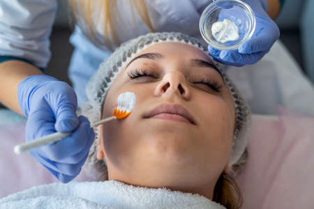 Cosmetologist applying healing cream on female client face skin in beauty clinic. healthcare