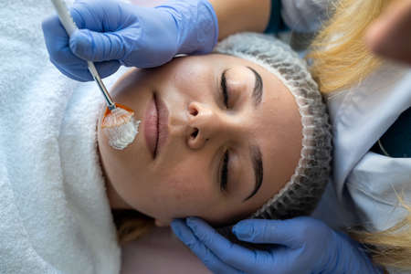 Cosmetologist applying healing cream on female client face skin in beauty clinic. healthcareの写真素材