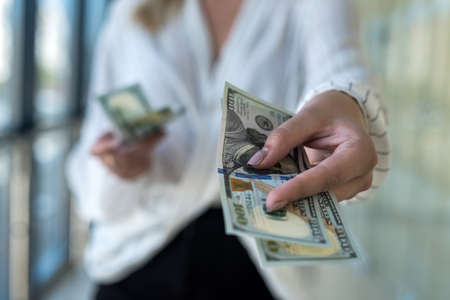 Female hands counting US dollar bills or paying in cash standing at modern business center or mall