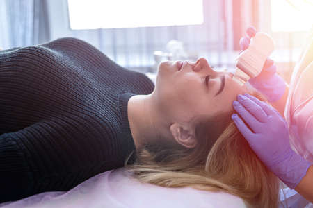 beautician in blue gloves makes a procedure of ultrasonic cleaning face to young female patient....