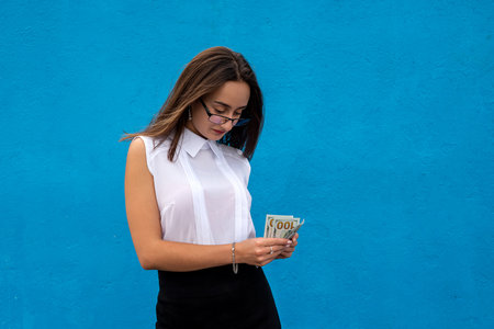portrait of young success business woman hold lot of money dollar bills isolated on blue