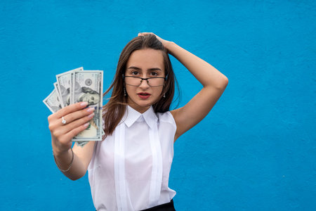 portrait of young success business woman hold lot of money dollar bills isolated on blueの写真素材