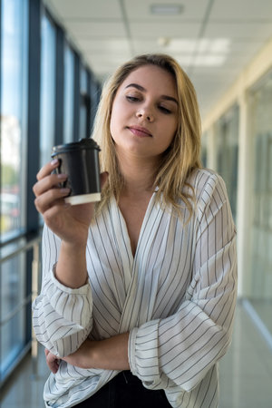 beautiful young woman enjoys coffee and listens to music during lunch break in the corridor of a...