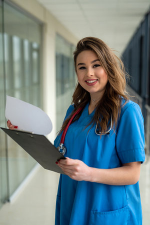 portrait of beautiful nurse in blue uniform with clipboard in modern hospital. medical conceptの写真素材
