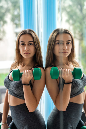 young slim woman working out with dumbbell while standing in front of window at gym. healthy lifestyleの写真素材