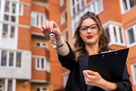 estate agent holding key against new house as background. sale conceptの写真素材