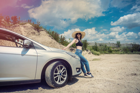 young pretty girl posing near the car in a sand quarry during a summer tripの写真素材