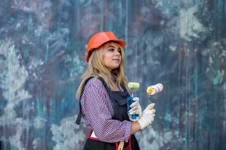 happy young woman in uniform holding paint roller near color wall. Home decoration conceptの写真素材