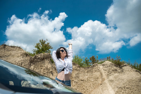 young pretty girl posing near the car in a sand quarry during a summer tripの写真素材