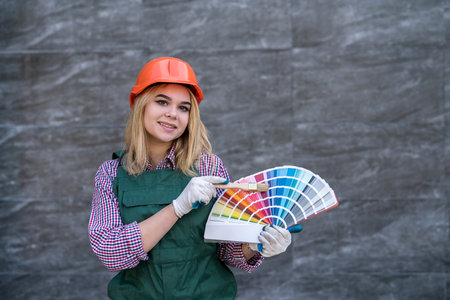 pretty woman in helmet and uniform ready for home repair, holding color palette. house designの写真素材
