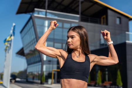 Pretty sports female model doing morning stretching in front of modern glass building, lifestyleの写真素材