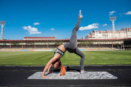 Sporty young female athlete stretching legs at the city stadium, healthy lifestyle