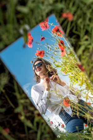 beautiful reflection of a girl in the mirror on a poppy field. summertimeの写真素材