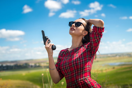 Sexy slender girl in a red dress holding a gun at nature, summer lifestyleの写真素材