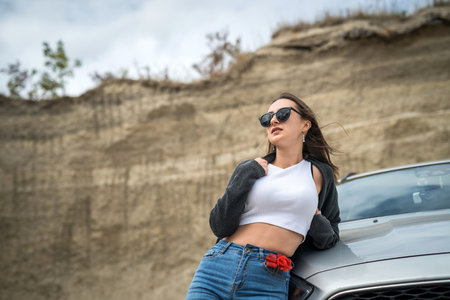 young pretty girl posing near the car in a sand quarry during a summer trip