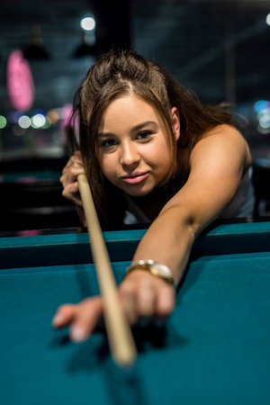 Young happy girl holding cue and play billiard at pub. lifestyle