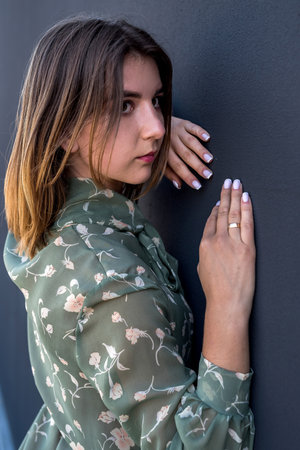 Calm beautiful young woman in elegant green dress near black wall. fashion female portrait