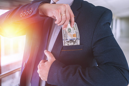 Man in blue suit and red tie putting bribe dollar bills into his pocket. corruption conceptの写真素材