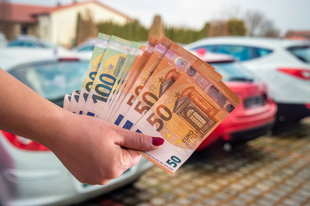 hands of a young woman holding a euro banknote on a background of cars. Wealth concept. car buying conceptの写真素材